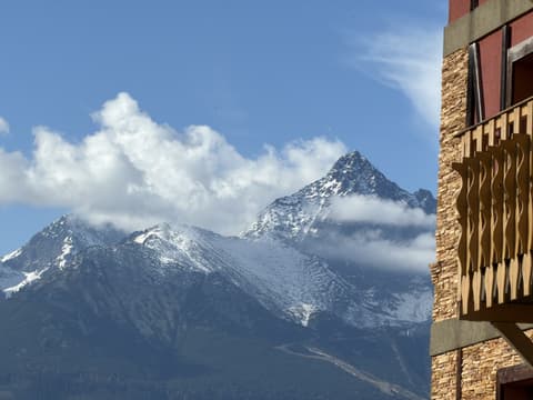 The pointed summit of Lomnický štít in fresh snow next to a carved balcony of the building